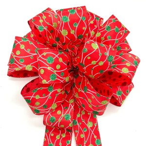 May include: A red and green Christmas bow with a white background. The bow is made of ribbon with a pattern of green and gold polka dots and white lines.