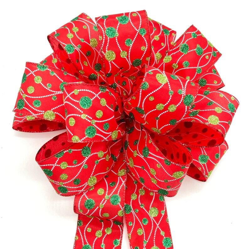 May include: A red and green Christmas bow with a white background. The bow is made of ribbon with a pattern of green and gold polka dots and white lines.
