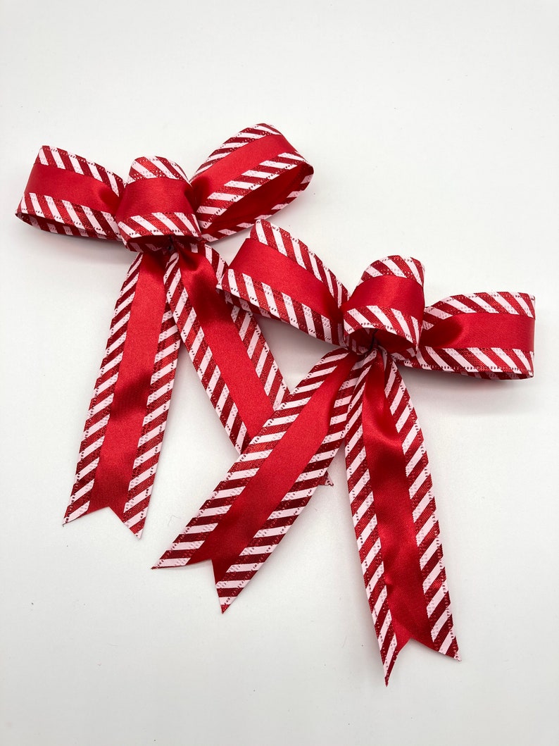 May include: Two red and white striped bows with a satin finish. The bows are tied together and are ready to be used for decorating.