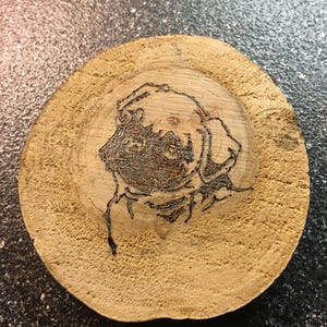 May include: A wood slice with a burnt image of a dog's head.
