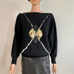 Può includere: Maglione nero con un design di paillettes dorate e argentate. Il maglione ha un collo a barca e maniche lunghe.