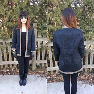 May include: A black quilted jacket with a floral trim. The jacket has a long, relaxed fit and a shawl collar. The model is wearing the jacket with black leggings and boots.