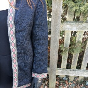 May include: A black quilted jacket with a gold and red trim. The jacket has a floral pattern and is worn over a black top.