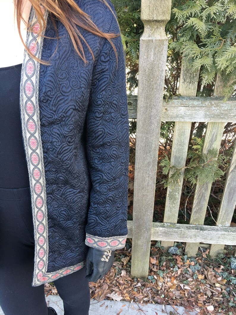 May include: A black quilted jacket with a gold and red trim. The jacket has a floral pattern and is worn over a black top.