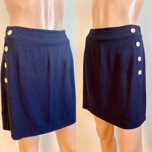 Op de afbeelding: Een donkerblauwe rok met een hoge taille en een rij gouden knopen aan de zijkant. De rok is gemaakt van een gladde, lichte stof.