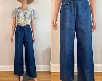 Può includere: Un paio di jeans di denim blu a gamba larga e vita alta con chiusura a bottone e una sola tasca sul lato destro.
