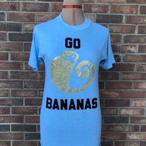 Camiseta vintage anos 80 azul bebê GO BANANAS com macaco pintado à mão dourado e letras de veludo flocadas em ferro tamanho M