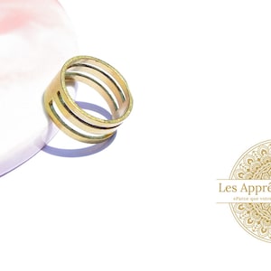 May include: A gold-toned ring with a double band design. The ring is on a pink and white surface.