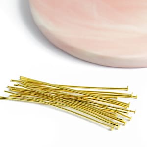 Peut inclure: Un tas d'épingles à tête dorées, également connues sous le nom d'épingles à tête pour la fabrication de bijoux, avec une tête plate à une extrémité. Les épingles sont disposées en un tas lâche sur une surface blanche.