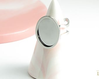 May include: A silver ring with a round, blank, silver-toned bezel. The ring is on a white and pink cone-shaped stand.