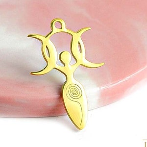 Puede incluir: Encanto de metal dorado con una figura femenina estilizada con tres lunas crecientes sobre su cabeza. La figura está de pie con los brazos levantados y un diseño en espiral en su torso.