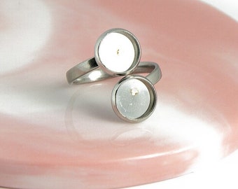 Puede incluir: Un anillo de plata con dos cabujones redondos de vidrio transparente. El anillo está sobre una superficie de mármol rosa y blanco.