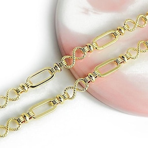 Op de afbeelding: Een gouden ketting met een delicaat, gedraaid ontwerp. De ketting is gemaakt van ovale schakels en wordt getoond op een roze en witte achtergrond.