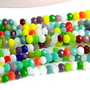 Può includere: Un filo di perline di vetro sfaccettate colorate in varie tonalità di rosso, verde, blu, giallo, bianco e viola. Le perline sono piccole e di dimensioni uniformi.