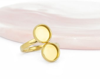 Puede incluir: Anillo de oro con dos engastes redondos vacíos. El anillo está sobre una superficie de mármol rosa y blanco.