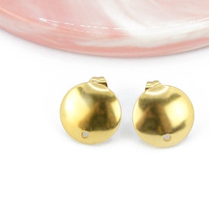 Op de afbeelding: Twee ronde oorbel-bevindingen in goudkleur met een klein gaatje in het midden. De bevindingen liggen op een wit oppervlak.