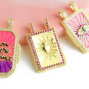 Peut inclure: Trois pendentifs dorés de forme rectangulaire. L'un porte l'inscription "Love is the Answer" en noir, sur fond rose et violet. Un autre présente un cœur avec des rayons de soleil. Le troisième a un motif d'œil.