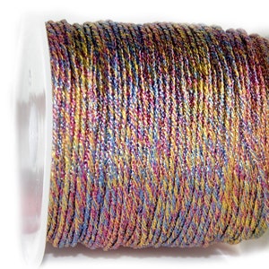 Op de afbeelding: Een spoel met metallic draad in een regenboog van kleuren, waaronder goud, rood, blauw en paars. De draad is gewikkeld om een witte plastic spoel.