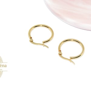 Könnte beinhalten: Ein Paar goldene Creolen mit einem Scharnierverschluss. Die Ohrringe befinden sich auf einem weißen Hintergrund.