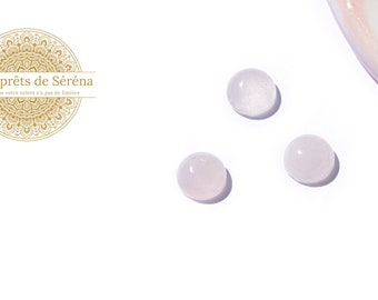 May include: Three small, round, translucent, light pink beads on a white background. The beads are smooth and have a slight sparkle.