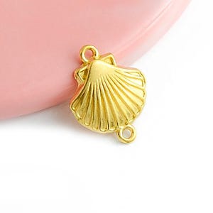 May include: Gold-toned seashell charm with two jump rings. The seashell has a detailed, textured design.