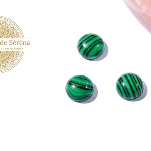 Puede incluir: Tres cabujones redondos de malaquita verde y negra sobre una superficie blanca.
