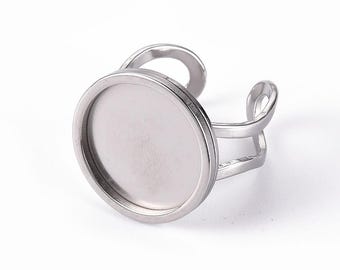 Puede incluir: Un anillo base de metal plateado con un engaste circular y un centro plano y hundido. La banda está abierta y dividida en dos brazos paralelos y curvos que se conectan a los lados de la bandeja circular, creando un diseño sencillo y estructural.