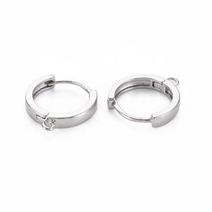 Puede incluir: Un par de pendientes de aro de plata con cierre de bisagra y un pequeño aro de salto en un lado.