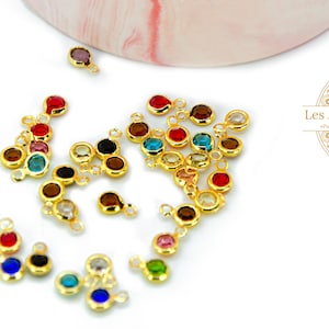 Pode incluir: Uma coleção de pingentes de metal dourado com pedras de vidro coloridas. Cada pingente tem um laço para prender a um colar, pulseira ou outra joia.