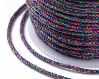 May include: A spool of multi-coloured braided cord. The cord is a mix of blue, green, and pink threads, tightly woven together. The cord is wound around a white plastic spool, with some cord unwound. Suitable for crafts and DIY projects.