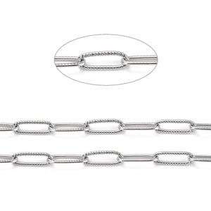 Könnte beinhalten: Nahaufnahme einer silbernen Kette mit ovalen Gliedern. Jedes Glied hat ein strukturiertes Muster an den Rändern und eine glatte, polierte Mitte. Die Kette wird vor einem weißen Hintergrund präsentiert, der den metallischen Glanz und das komplizierte Design hervorhebt.