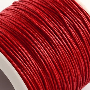 Könnte beinhalten: Nahaufnahme einer Spule aus leuchtend roter, gewachster Baumwollschnur. Die Schnur ist eng gewickelt und zeigt eine strukturierte Oberfläche. Der weiße Spulenrand ist in der unteren linken Ecke sichtbar. Diese Schnur eignet sich für verschiedene Bastelprojekte.