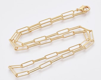 Puede incluir: Collar de cadena de clip de papel de color dorado con cierre de mosquetón. La cadena está hecha de eslabones rectangulares alargados. El collar se muestra sobre una superficie blanca.
