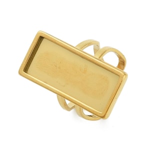 Könnte beinhalten: Ein goldfarbener Ring mit rechteckiger Oberfläche. Der Ring hat eine erhöhte Lünette um die Oberfläche, die einen Rahmen bildet. Das Band hat ein Mehrfachschlaufendesign. Der Ring ist vor weißem Hintergrund.