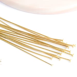 Puede incluir: Primer plano de un montón de alfileres de cabeza dorados. Los alfileres miden aproximadamente 5 cm de largo y tienen un pequeño bucle en la parte superior.