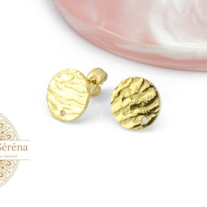 May include: A pair of gold-toned earrings with a textured, circular design. The earrings have a small hole in the center of each circle.