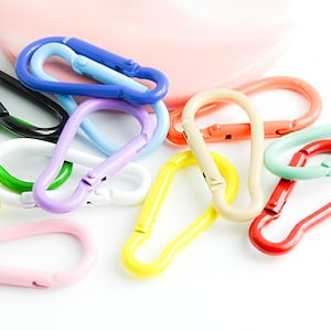 May include: A collection of colorful metal keychains in various shades of blue, green, yellow, pink, red, and white. The keychains are shaped like a simple loop with a clasp.
