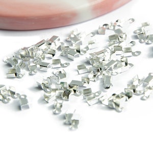 Op de afbeelding: Een stapel zilverkleurige metalen sluitingen voor het maken van sieraden. De sluitingen zijn klein en hebben een rechthoekige vorm met een kleine lus aan elk uiteinde.
