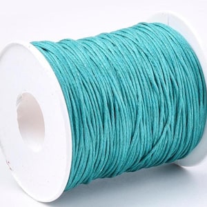 Op de afbeelding: Een spoel turquoise gewaxt katoenen koord. Het koord is gewikkeld rond een witte plastic spoel. Het koord heeft een glad uiterlijk en een lichte glans. Dit koord is geschikt voor het maken van sieraden, knutselen en andere creatieve projecten.