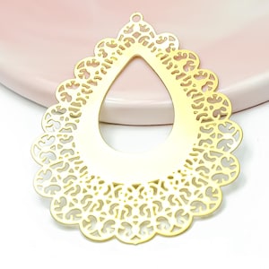 Peut inclure: Un pendentif en métal doré en forme de goutte avec un motif ajouré en filigrane détaillé. La pièce présente un bord festonné et une petite boucle circulaire au sommet pour la fixation, mettant en valeur une finition de surface plate et polie.