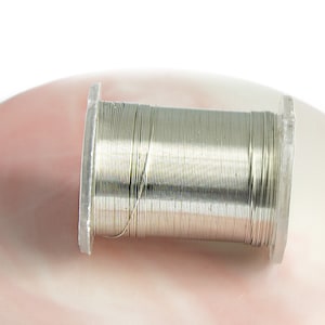 Può includere: Un rotolo di filo color argento, avvolto strettamente e pronto per progetti di artigianato.