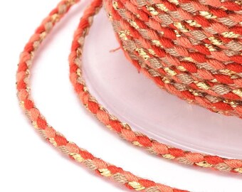 May include: A close-up of a spool of coral and beige braided cord with gold metallic thread woven throughout. The cord is twisted and has a subtle sheen.