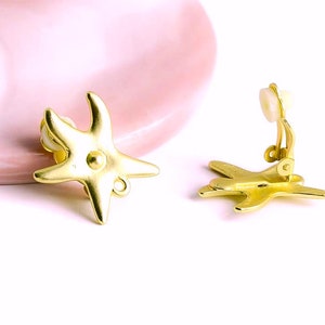 Peut inclure: Boucles d'oreilles clips dorées en forme d'étoile de mer. Les boucles d'oreilles ont un design simple et élégant, parfait pour ajouter une touche de fantaisie à n'importe quelle tenue.