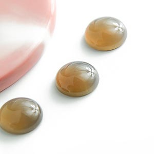 Peut inclure: Trois pierres précieuses rondes, brunes et grises, en cabochon, avec un léger éclat iridescent.