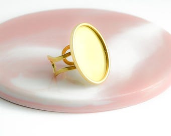 Puede incluir: Engaste de anillo de oro con una bandeja redonda, en blanco, con bisel. El engaste está sobre una superficie de mármol rosa y blanco.