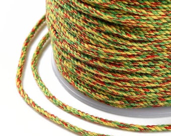 May include: A close-up shot of a spool of multi-coloured braided cord. The cord is a mix of red, green, and yellow, tightly wound on a clear plastic spool. The braided texture is visible, with vibrant colours.