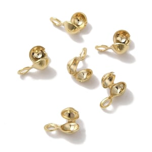 Könnte beinhalten: Mehrere goldfarbene Quetschhülsen-Endkappen liegen auf einer weißen Oberfläche. Jede Kappe hat eine kleine Schlaufe und einen geteilten, abgerundeten Körper. Einige sind geöffnet und zeigen das Innere.