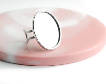 Puede incluir: Un aro de anillo en plata con un bisel redondo de forma ovalada. El aro de anillo está sobre una superficie de mármol rosa y blanco.