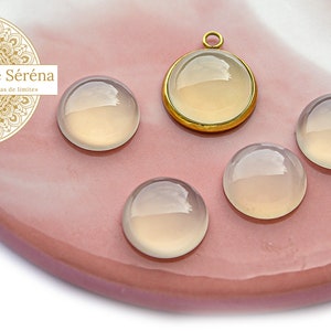 Peut inclure: Cinq cabochons ronds, translucides, blancs avec un sertissage en métal doré. Les cabochons sont disposés en demi-cercle avec le sertissage au centre.