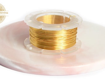 Pode incluir: Um carretel de fio dourado em uma superfície de mármore branco e rosa. O fio está em um dispensador de plástico transparente.